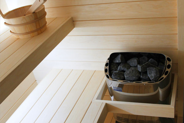 Interno di una sauna finlandese in legno chiaro con stufa elettrica, pietre e panche